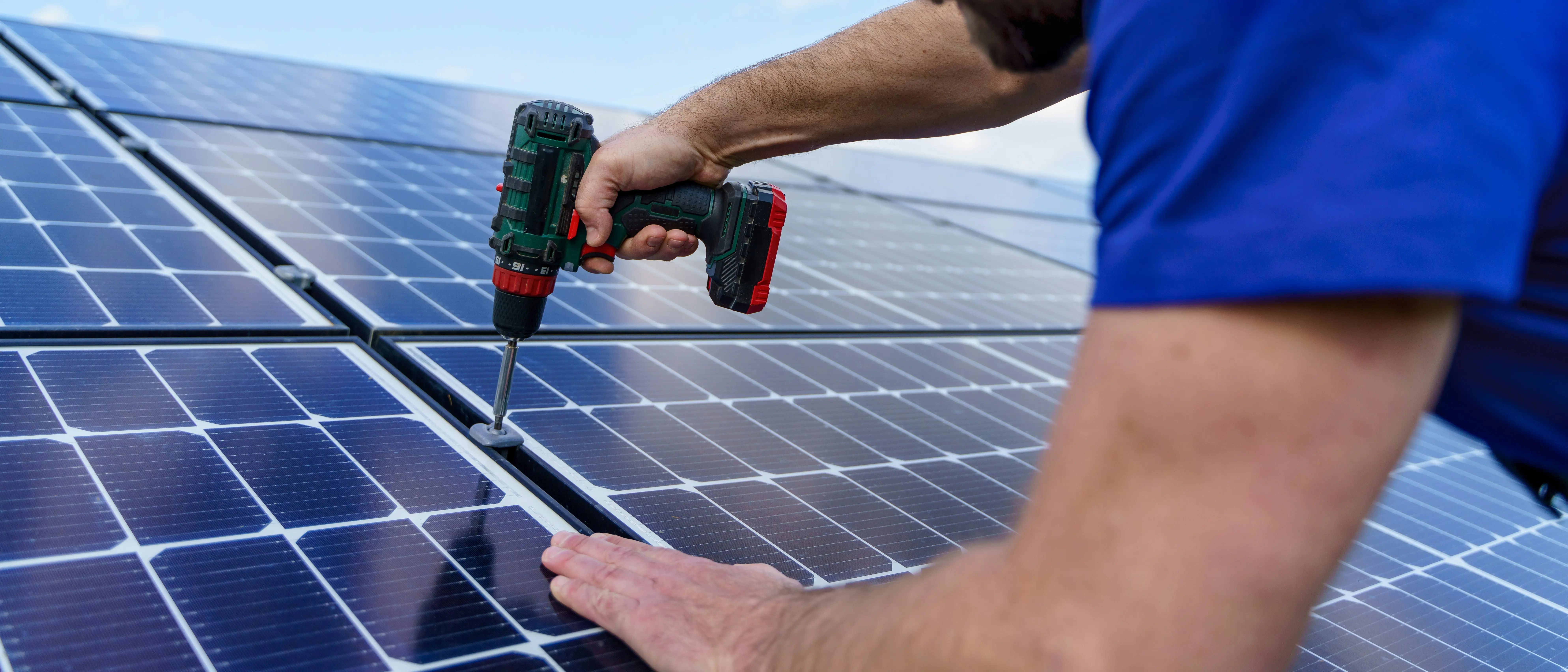 Person uses a power drill to install or secure a solar panel on a rooftop solar array.