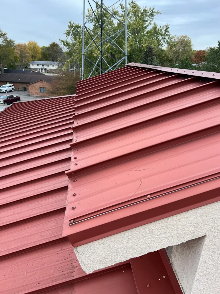 The edge of a red metal roof with trees in the background